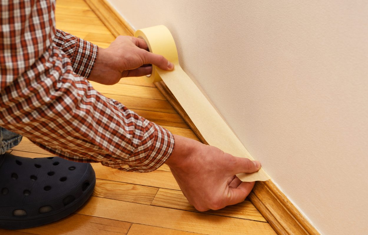 Preparing a room for painting walls. Master painter glues the masking tape on the baseboard. Repair in the house