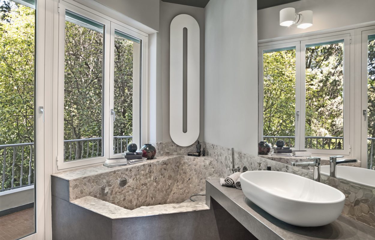 Interior view of a modern bathroom in the foreground the washbasin on the masonry top and in the corner on the background under the window there is the masonry bathtub