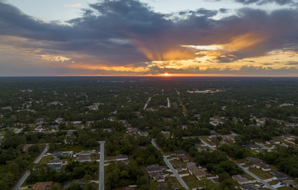 Aerial view of suburban landscape with private homes between green palm trees in Florida quiet residential area in evening.