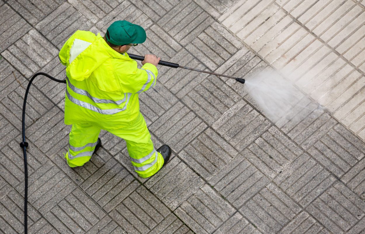 Worker cleaning a pavement sidewalk with high pressure water jet. Maintenance of public areas